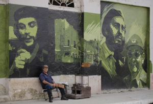 A man waits for customers at his shoe-cleaning stall beside a mural with images of revolution leader Che Guevara, (L), former Cuban leader Fidel Castro and current President Raul Castro, (R), in Sagua La Grande, around 240 km (149 miles) east of Havana, in the province of Villaclara in central Cuba December 14, 2011. REUTERS/Desmond Boylan (CUBA - Tags: SOCIETY POLITICS)
